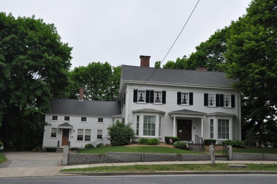 White clapboard Deacon Willard Lewis House with trees and a stone wall in Walpole, Massachusetts